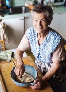 Picture of elderly woman in a blue dress mixing ingredients together in a bowl.